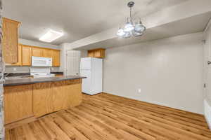 Kitchen featuring light hardwood / wood-style floors, an inviting chandelier, kitchen peninsula, sink, and white appliances