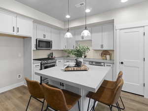 Kitchen featuring light hardwood / wood-style floors, white cabinets, hanging light fixtures, and appliances with stainless steel finishes