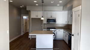 Kitchen with a kitchen island, white cabinetry, appliances with stainless steel finishes, decorative light fixtures, and dark hardwood / wood-style flooring