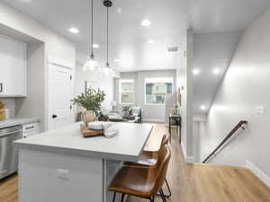 Kitchen featuring white cabinets, decorative light fixtures, stainless steel dishwasher, and light hardwood / wood-style flooring