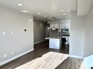 Kitchen featuring stainless steel appliances, hanging light fixtures, a kitchen island, and dark hardwood / wood-style flooring