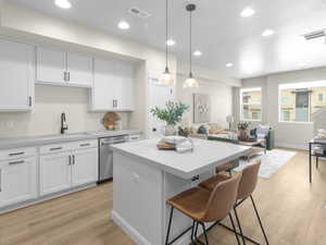 Kitchen featuring white cabinetry, sink, hanging light fixtures, stainless steel dishwasher, and light wood-type flooring