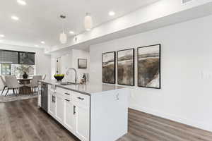 Kitchen with white cabinets, a center island with sink, decorative light fixtures, and dark hardwood / wood-style flooring