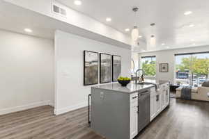 Kitchen featuring decorative light fixtures, an island with sink, white cabinets, dark wood-type flooring, and stainless steel dishwasher