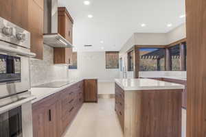 Kitchen with stainless steel double oven, backsplash, black electric cooktop, wall chimney exhaust hood, and a center island