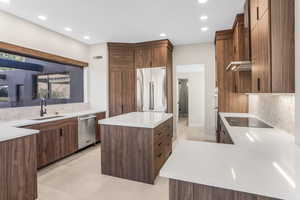 Kitchen with stainless steel appliances, sink, tasteful backsplash, a center island, and wall chimney range hood