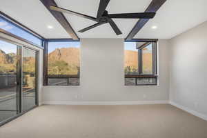 Carpeted empty room with a mountain view, ceiling fan, and beam ceiling