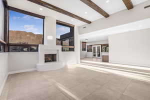 Unfurnished living room featuring light tile patterned flooring, beam ceiling, a large fireplace, a mountain view, and french doors