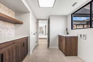 Bar featuring sink, dark brown cabinetry, decorative backsplash, and light tile patterned floors