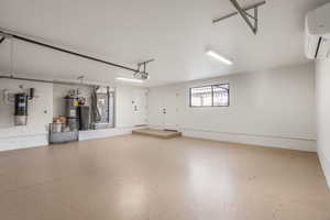 Garage with a garage door opener, heating unit, strapped water heater, and a wall mounted AC