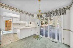 Kitchen with white cabinets, light carpet, decorative light fixtures, and kitchen peninsula