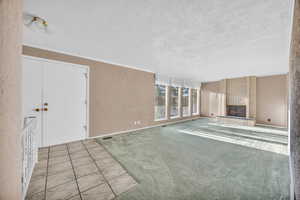 Unfurnished living room with a textured ceiling, light colored carpet, and a brick fireplace