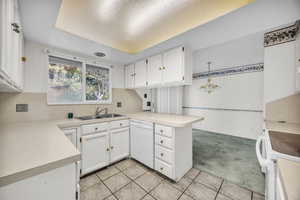 Kitchen featuring white appliances, sink, white cabinets, kitchen peninsula, and light colored carpet