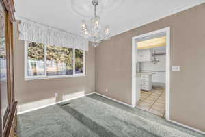 Carpeted empty room featuring a notable chandelier and crown molding