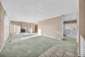 Unfurnished living room with a textured ceiling, light carpet, crown molding, and a brick fireplace