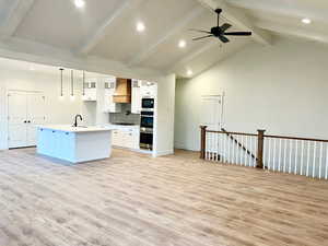 Kitchen with sink, light hardwood / wood-style flooring, an island with sink, decorative light fixtures, and white cabinets