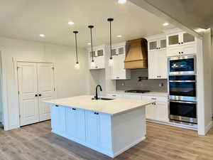 Kitchen with light hardwood / wood-style floors, custom range hood, an island with sink, and appliances with stainless steel finishes