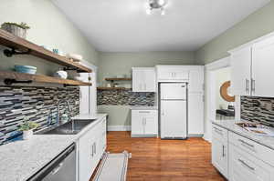 Kitchen with light hardwood / wood-style floors, sink, white cabinets, white refrigerator, and decorative backsplash