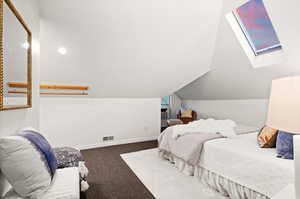 Bedroom featuring vaulted ceiling with skylight and dark colored carpet