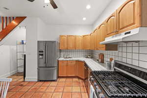 Kitchen featuring tile countertops, decorative backsplash, light tile patterned floors, ceiling fan, and appliances with stainless steel finishes