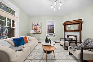 Living room featuring a stone fireplace, light wood-type flooring, cooling unit, and a notable chandelier