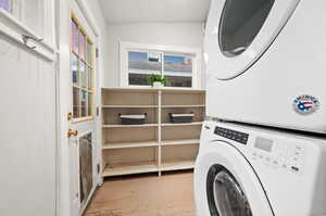 Laundry area with stacked washer and dryer and light wood-type flooring