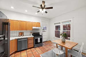 Kitchen with stainless steel appliances, tile countertops, ceiling fan, light tile patterned floors, and backsplash