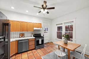 Kitchen with tile countertops, light tile patterned floors, tasteful backsplash, ceiling fan, and appliances with stainless steel finishes