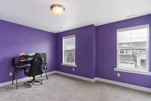 Carpeted office/bedroom space featuring plenty of natural light