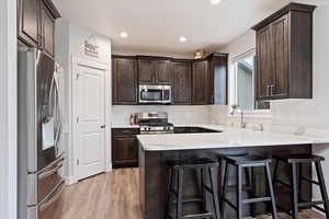 Kitchen featuring appliances with stainless steel finishes, dark brown cabinetry, light hardwood / wood-style floors, a breakfast bar, and kitchen peninsula