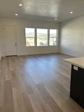 Unfurnished living room with a wealth of natural light, a textured ceiling, and light hardwood / wood-style floors