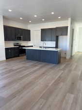 Kitchen with stainless steel appliances, light hardwood / wood-style floors, a center island with sink, and a textured ceiling