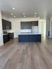 Kitchen with stainless steel appliances, light hardwood / wood-style floors, a center island with sink, sink, and decorative backsplash