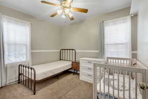 Carpeted bedroom with ceiling fan and lots of natural light