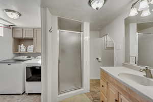 Bathroom with a textured ceiling, washer and clothes dryer, vanity, a shower with shower door, and tile patterned floors