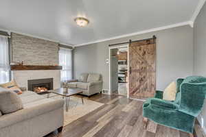 Living room featuring ornamental molding, hardwood / wood-style floors, a barn door, and a stone fireplace