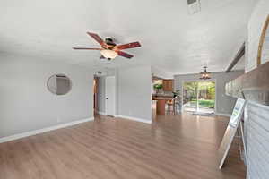 Unfurnished living room with ceiling fan with notable chandelier, light hardwood / wood-style flooring, a textured ceiling, and beam ceiling