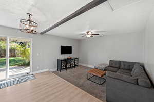 Living room featuring ceiling fan with notable chandelier, wood-type flooring, a textured ceiling, and beam ceiling