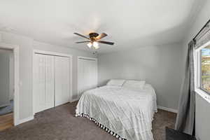 Carpeted bedroom featuring ceiling fan, a textured ceiling, and multiple closets