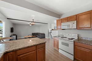 Kitchen featuring white appliances, light stone counters, ceiling fan, and light hardwood / wood-style flooring