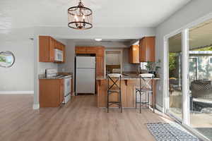 Kitchen featuring a chandelier, decorative light fixtures, light hardwood / wood-style floors, a kitchen breakfast bar, and white appliances