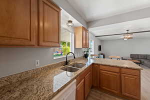 Kitchen with dishwasher, light stone countertops, kitchen peninsula, and sink