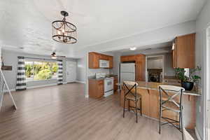 Kitchen with kitchen peninsula, a kitchen breakfast bar, light stone countertops, white appliances, and light hardwood / wood-style flooring