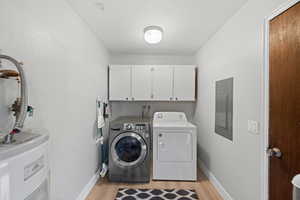 Washroom with separate washer and dryer, electric panel, cabinets, water heater, and light hardwood / wood-style flooring