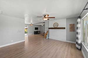 Unfurnished living room featuring light wood-type flooring, a textured ceiling, ceiling fan, and a fireplace