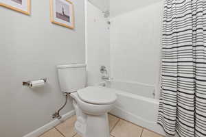 Bathroom featuring toilet, shower / tub combo with curtain, and tile patterned floors