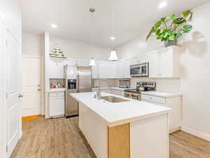 Kitchen with light hardwood / wood-style floors, a center island with sink, white cabinets, sink, and appliances with stainless steel finishes