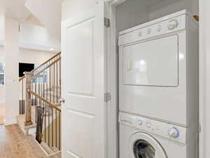 Clothes washing area with stacked washer and clothes dryer and hardwood / wood-style flooring