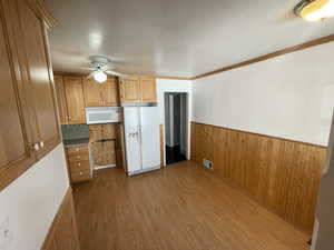 Kitchen featuring wood walls, ornamental molding, ceiling fan, light wood-type flooring, and white appliances