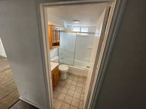 Full bathroom featuring tile patterned floors, enclosed tub / shower combo, vanity, a textured ceiling, and toilet